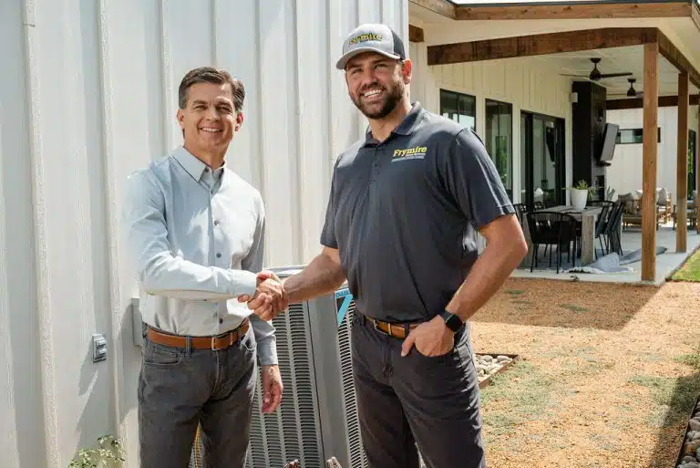 Homeowner and Frymire technician shaking hands and smiling while standing next to a building
