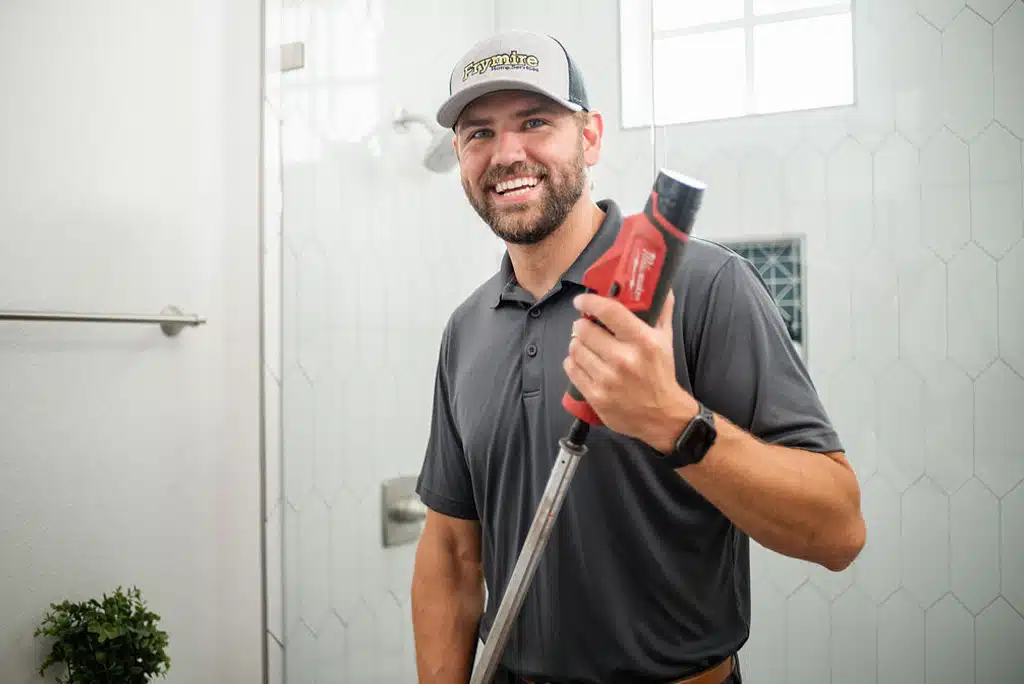 Frymire technician standing in front of a mirror using plumbing equipment to complete toilet repair in a home.