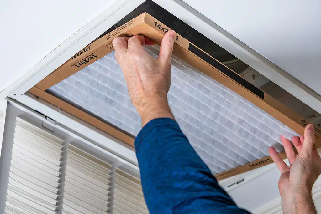Technician's hands putting a clean new air filter in a home's air vent in the ceiling.