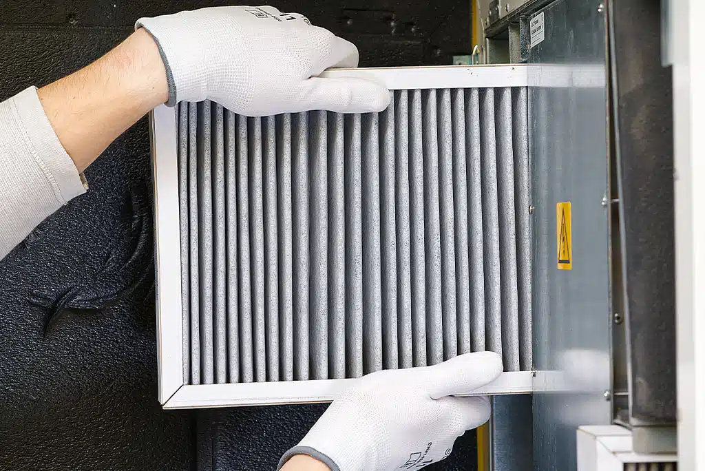 Technician's hands in white work gloves, pulling an air filter out of a home's HVAC system.