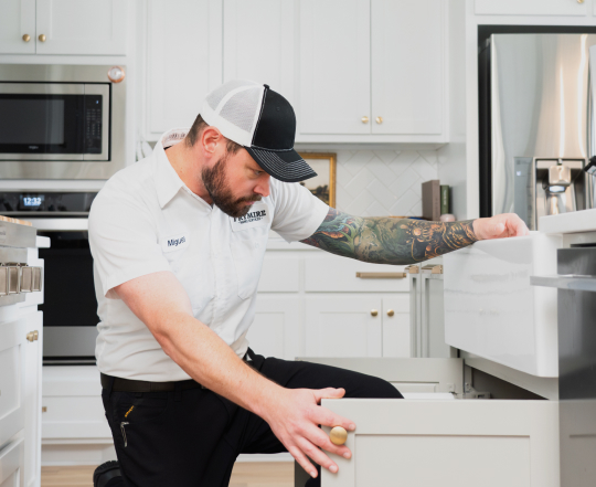 Technician in a kitchen, looking at pipes in cabinet under the sink.