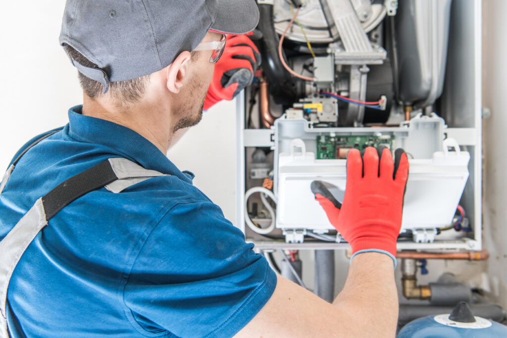 Technician maintaining a furnace while wearing red work gloves.