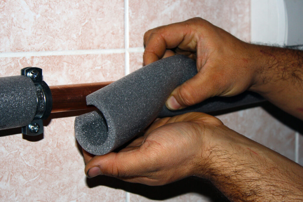 Worker cuts the foam insulation and fits it around copper pipes in a home.